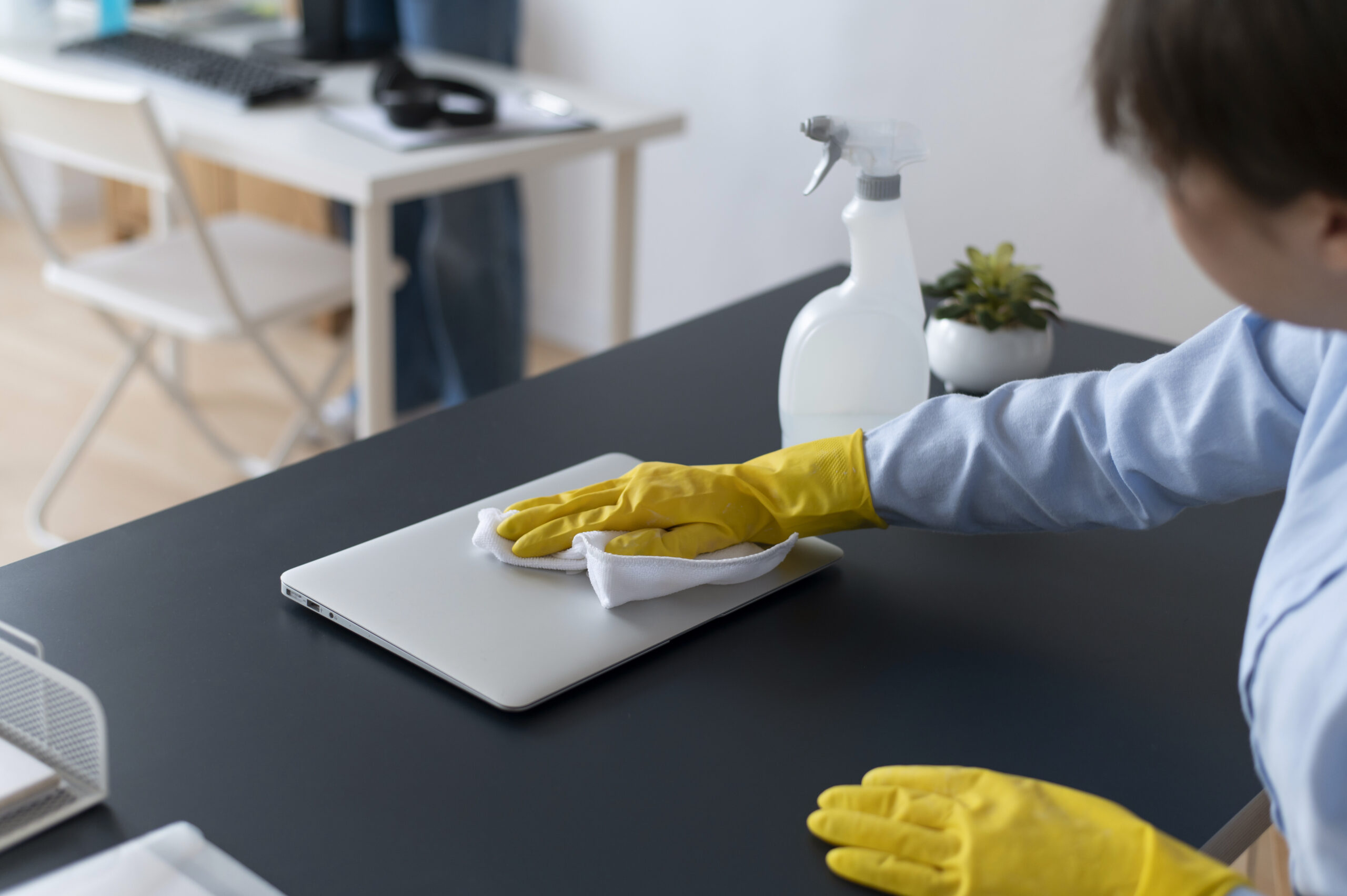 Cleaner wiping a laptop and desk during office cleaning in Manchester